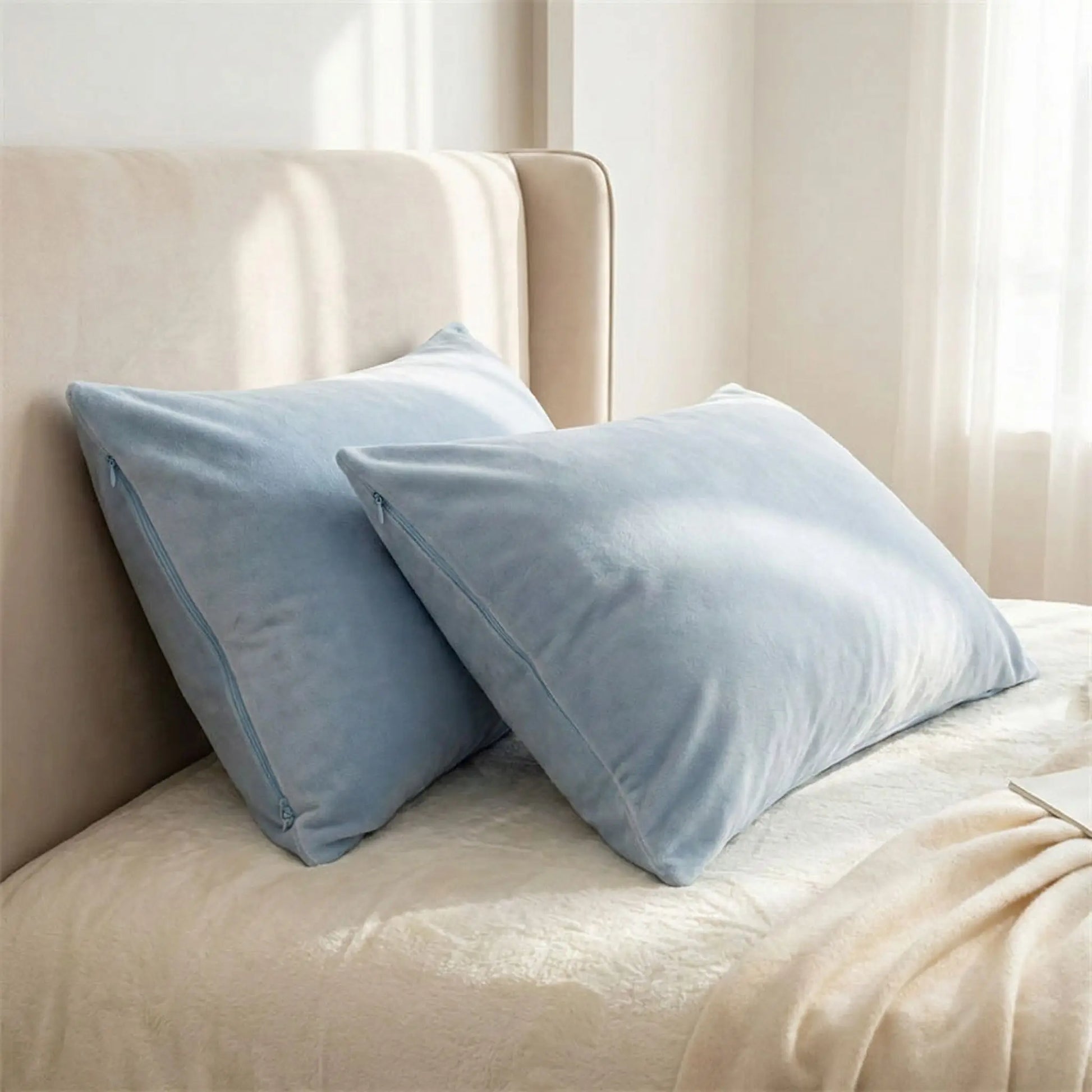Deux Taies d’oreiller en velours bleu ciel présentées seule sur un lit, texture veloutée et finition soignée