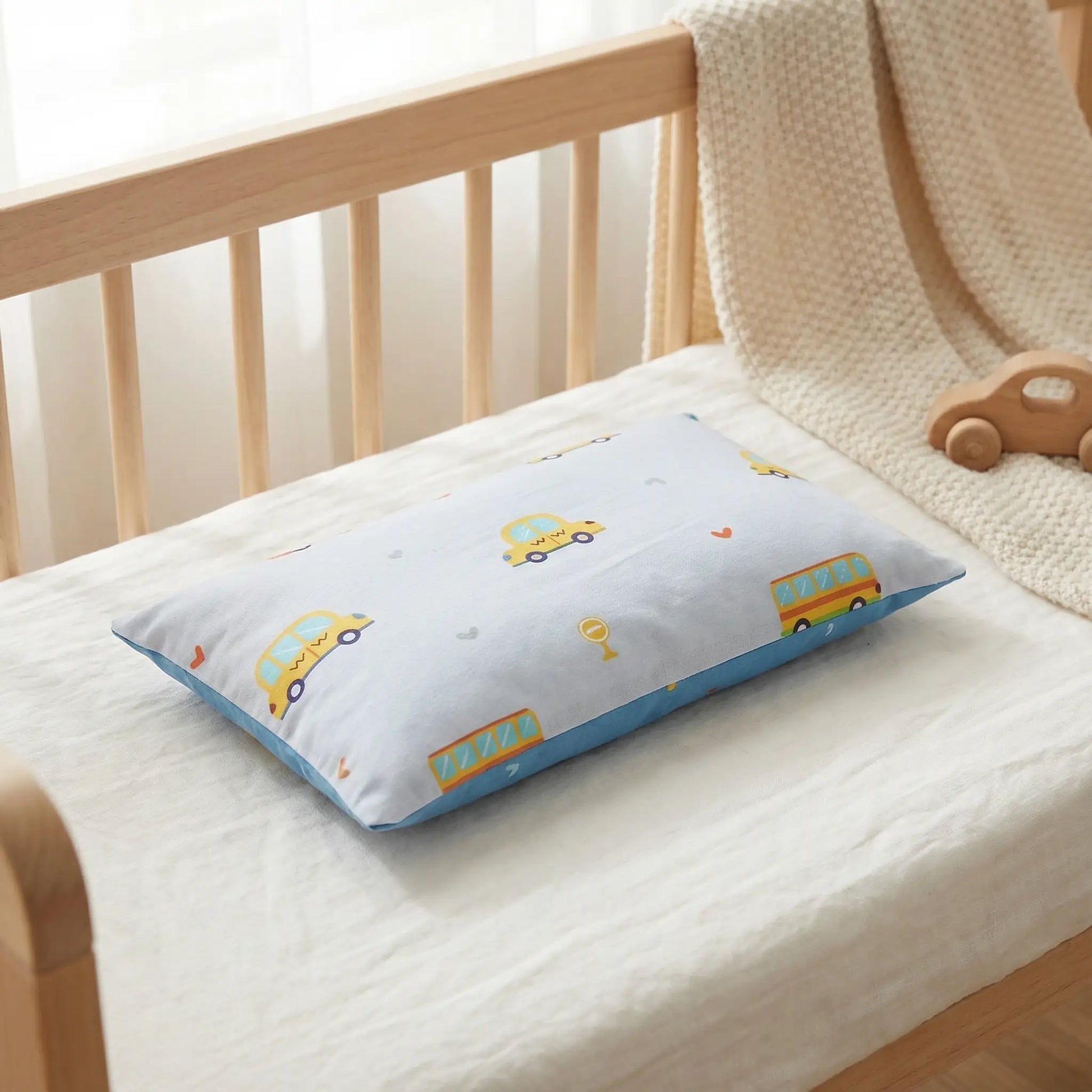 Taie d’oreiller bébé en coton à motif voitures présentée seule dans un berceau