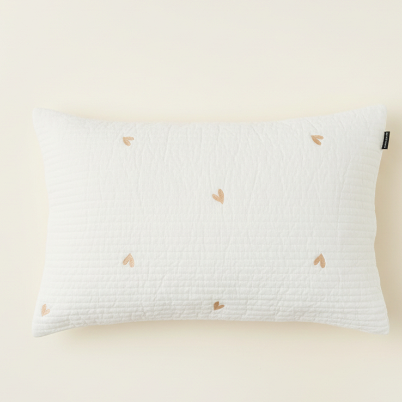 Taie d’oreiller bébé en coton matelassé à motif cœurs présentée seule sur fond clair