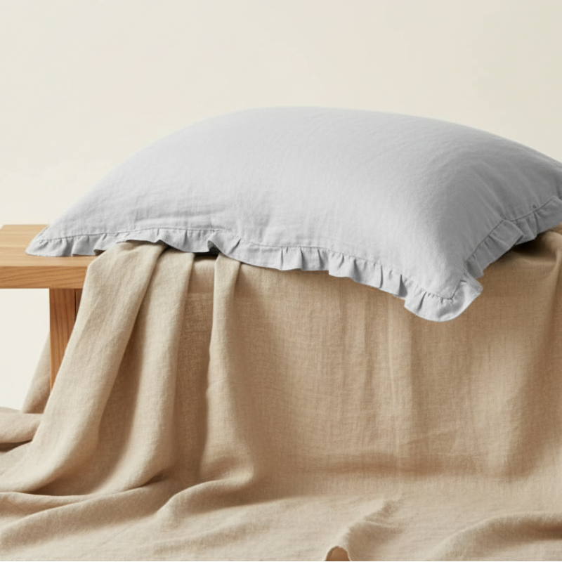 Taie d’oreiller en lin gris à volants présentée seule sur support beige