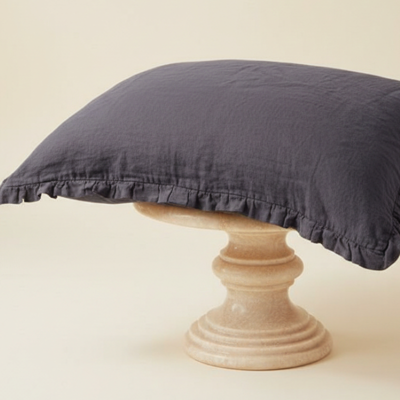 Taie d’oreiller en lin gris à volants présentée seule sur tabouret beige