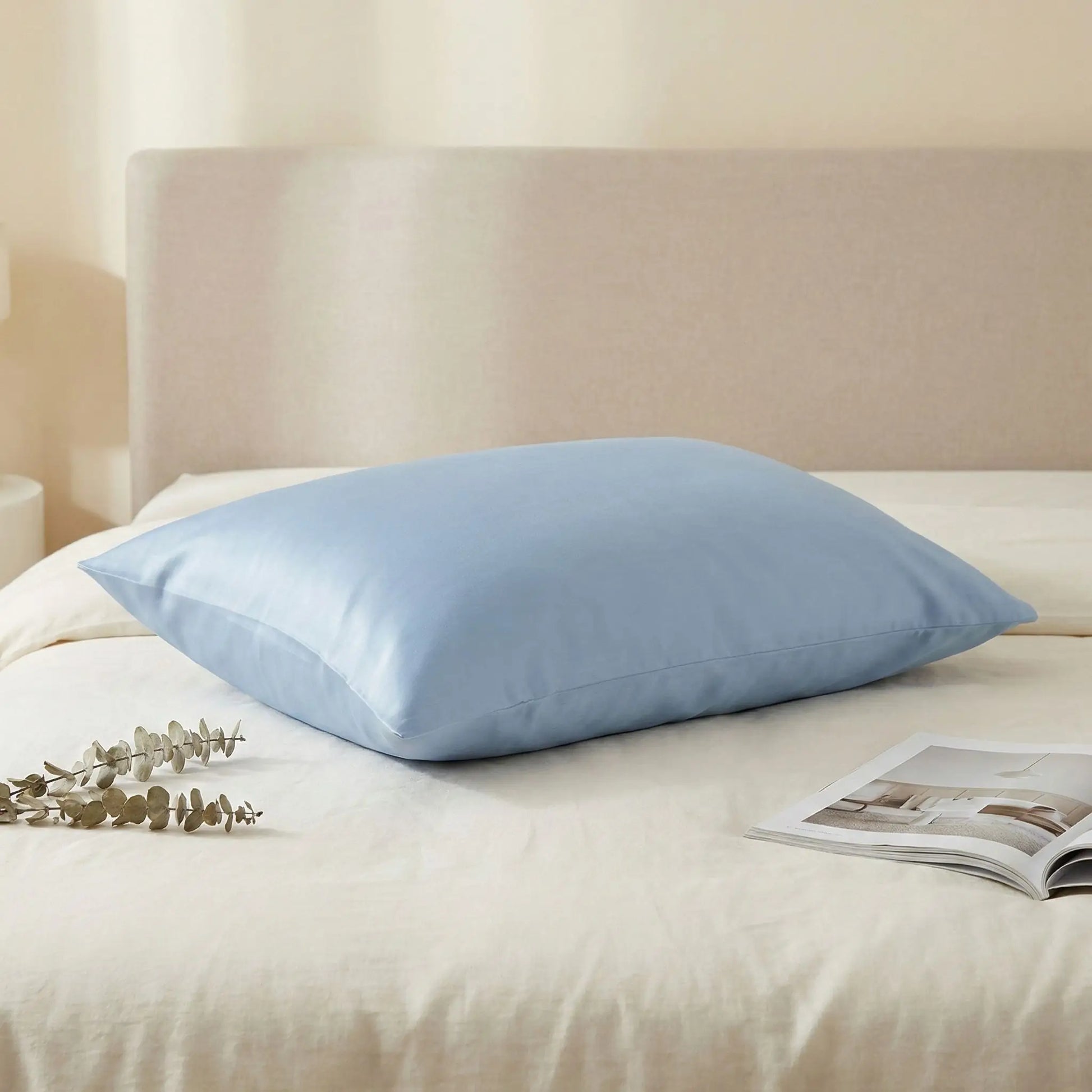 Taie d’oreiller en satin de coton bleu présentée seule sur un lit