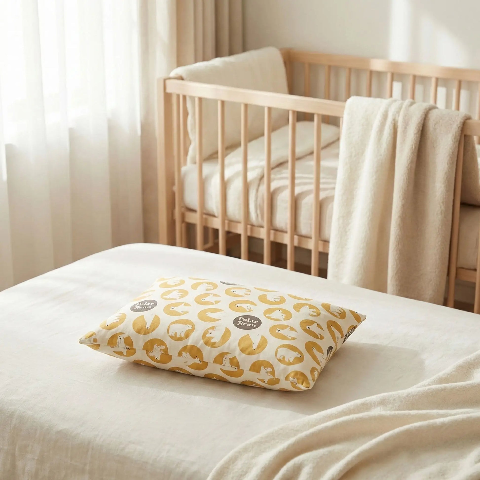 Taies d’oreiller bébé en coton à motif ours jaunes posées sur un lit bébé en bois clair avec linge de lit blanc cassé
