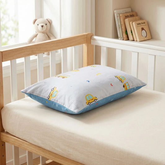 Taies d’oreiller bébé en coton à motif voitures posées sur un lit bébé en bois clair avec linge de lit blanc cassé