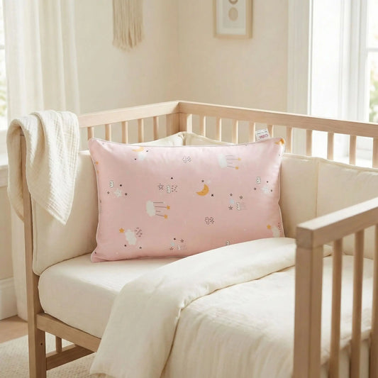 Taies d’oreiller bébé en coton rose posées sur un lit bébé en bois clair avec linge de lit blanc cassé