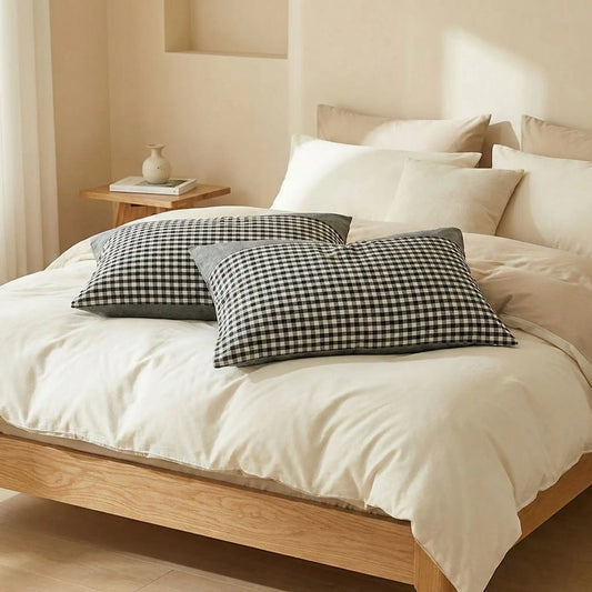 Taies d’oreiller en coton égyptien gris posées sur un lit en bois clair avec linge de lit blanc cassé