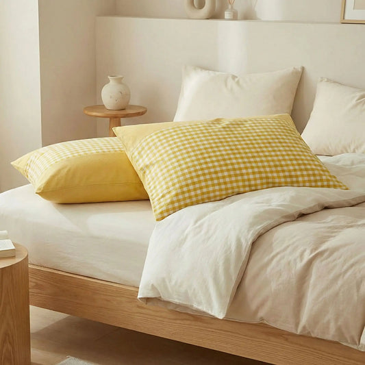 Taies d’oreiller en coton égyptien jaune posées sur un lit en bois clair avec linge de lit blanc cassé