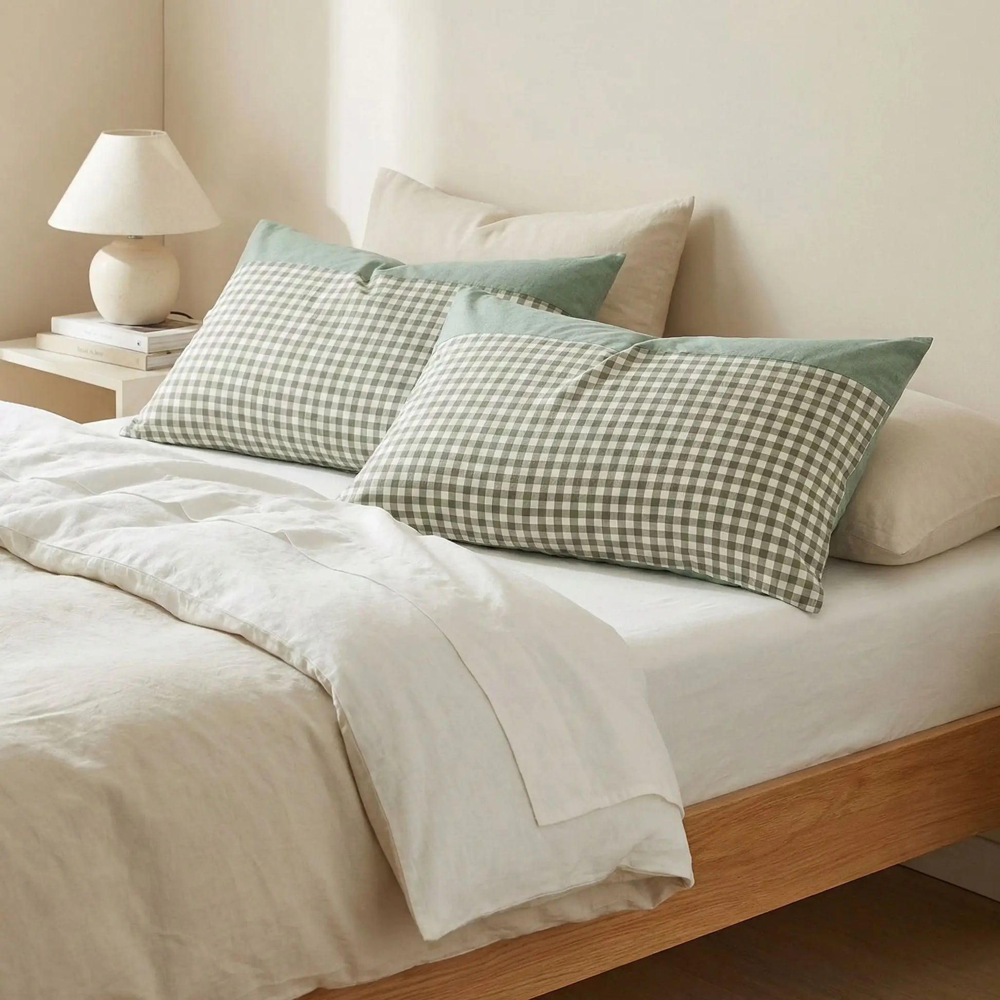 Taies d’oreiller en coton égyptien vert posées sur un lit en bois clair avec linge de lit blanc cassé