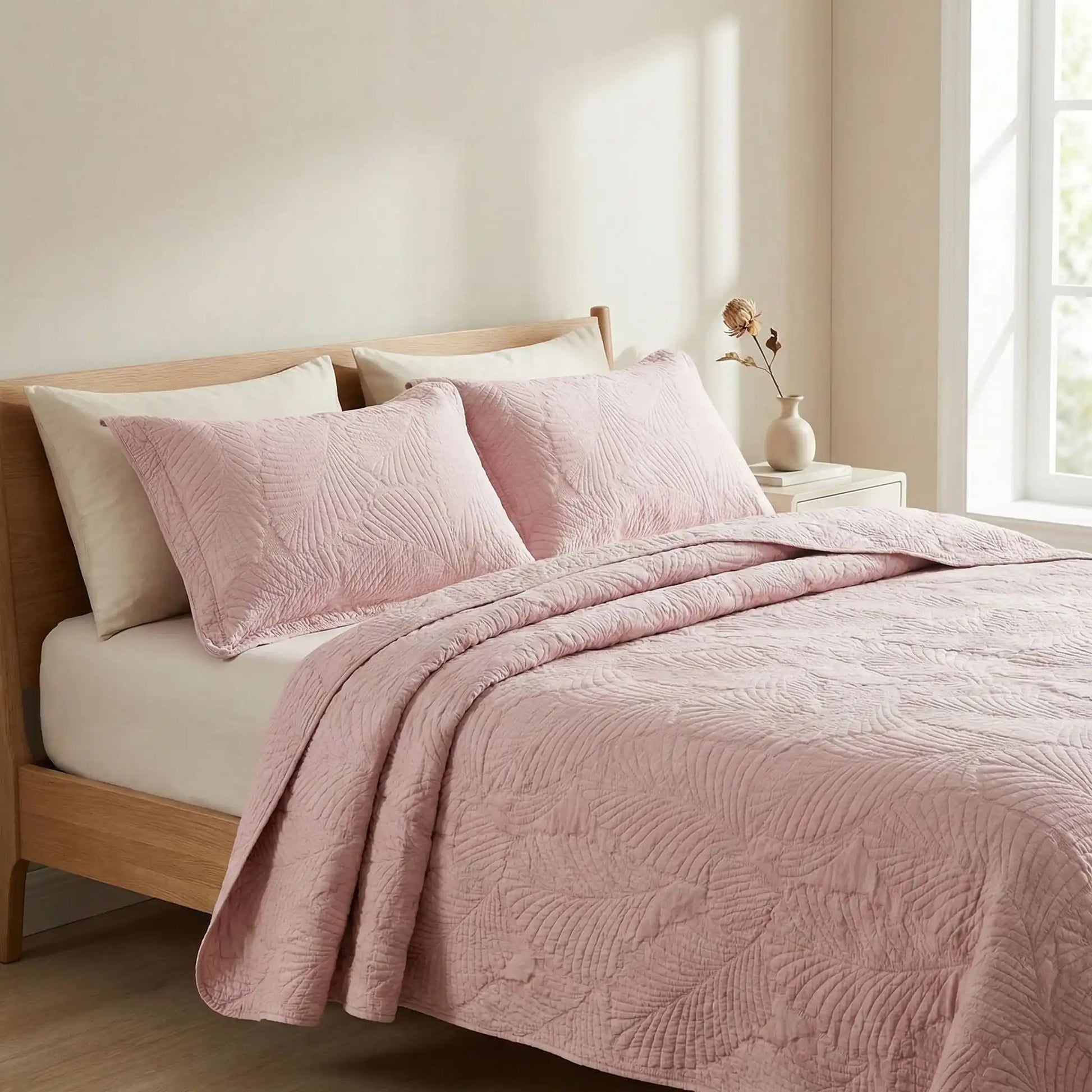 Taies d’oreiller en coton matelassé rose poudrée posées sur un lit en bois clair avec linge de lit rose