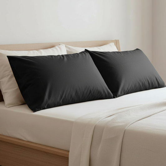 Taies d’oreiller en fibre d’eucalyptus noires posées sur un lit en bois clair avec linge de lit blanc cassé