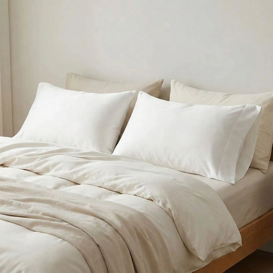 Taies d’oreiller en fibre de bambou blanches posées sur un lit en bois clair avec linge de lit blanc cassé