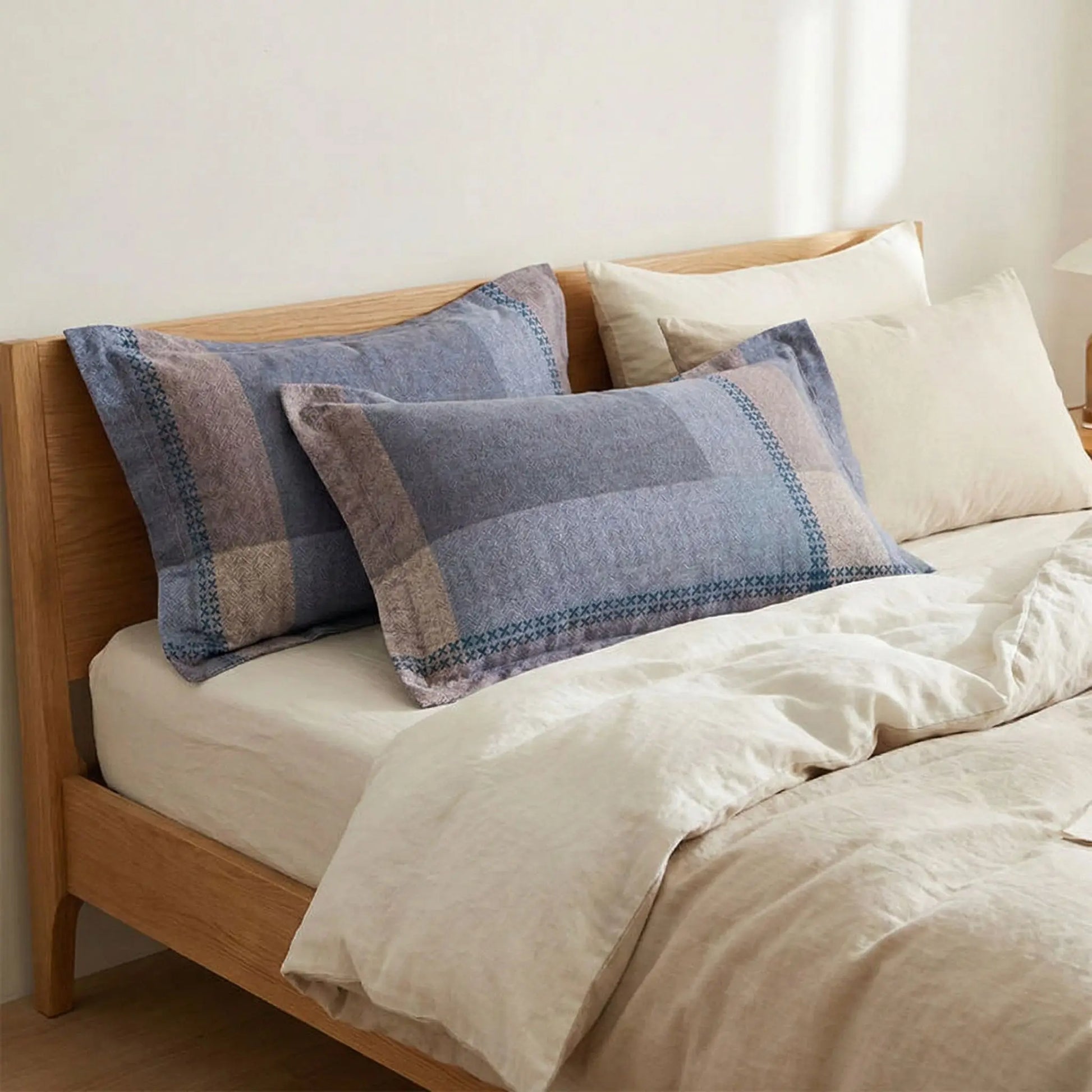 Taies d’oreiller en flanelle à motif bleu et marron posées sur un lit en bois clair avec linge de lit blanc cassé