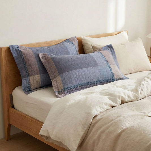 Taies d’oreiller en flanelle à motif bleu et marron posées sur un lit en bois clair avec linge de lit blanc cassé