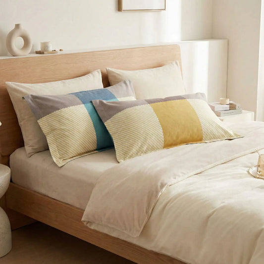 Taies d’oreiller en flanelle au design coloré jaune et bleu posées sur un lit en bois clair avec linge de lit blanc cassé