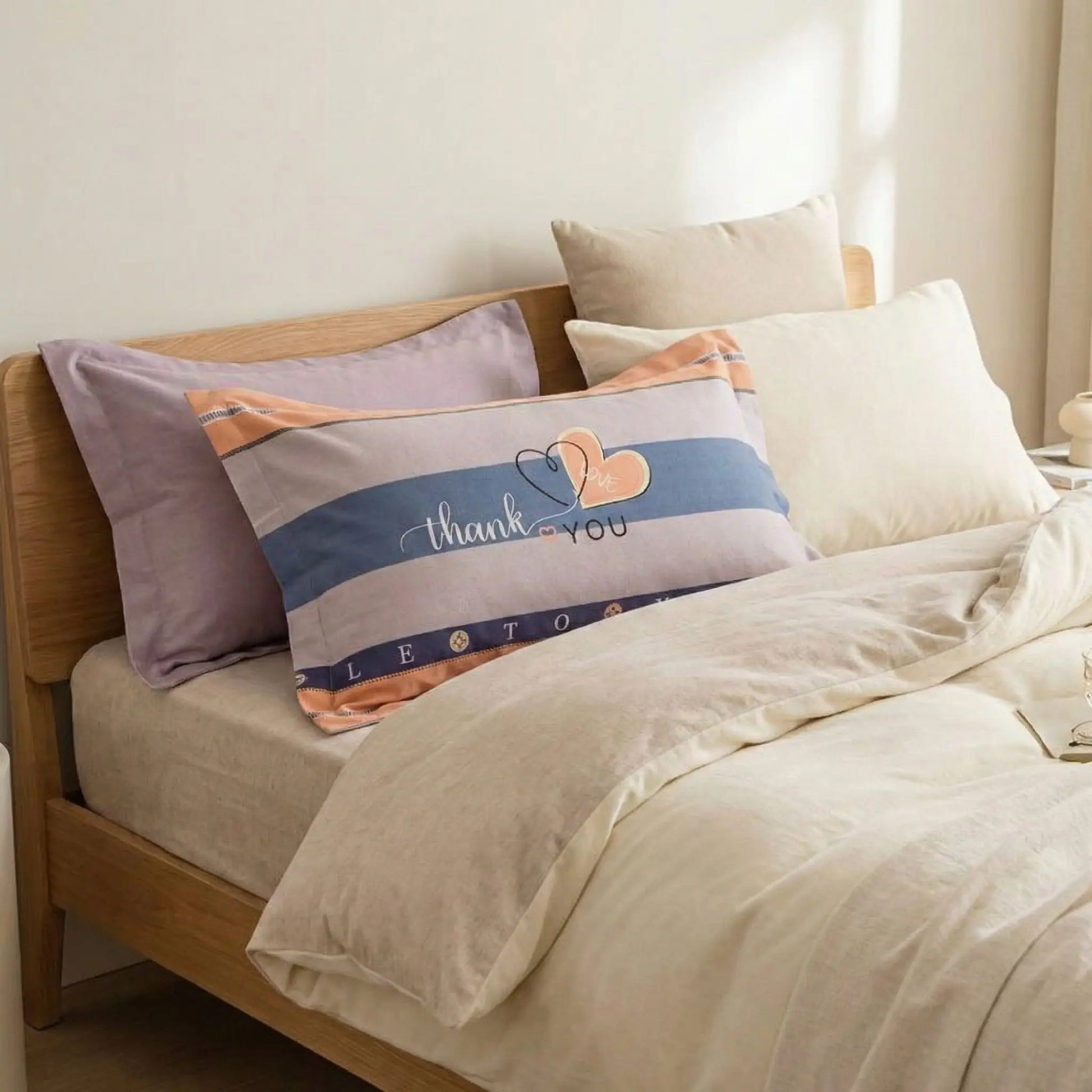 Taies d’oreiller en flanelle avec message Thank you posées sur un lit en bois clair avec linge de lit blanc cassé