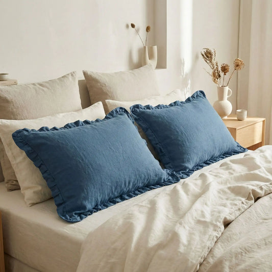 Taies d’oreiller en lin bleu à volants posées sur un lit en bois clair avec linge de lit blanc cassé 