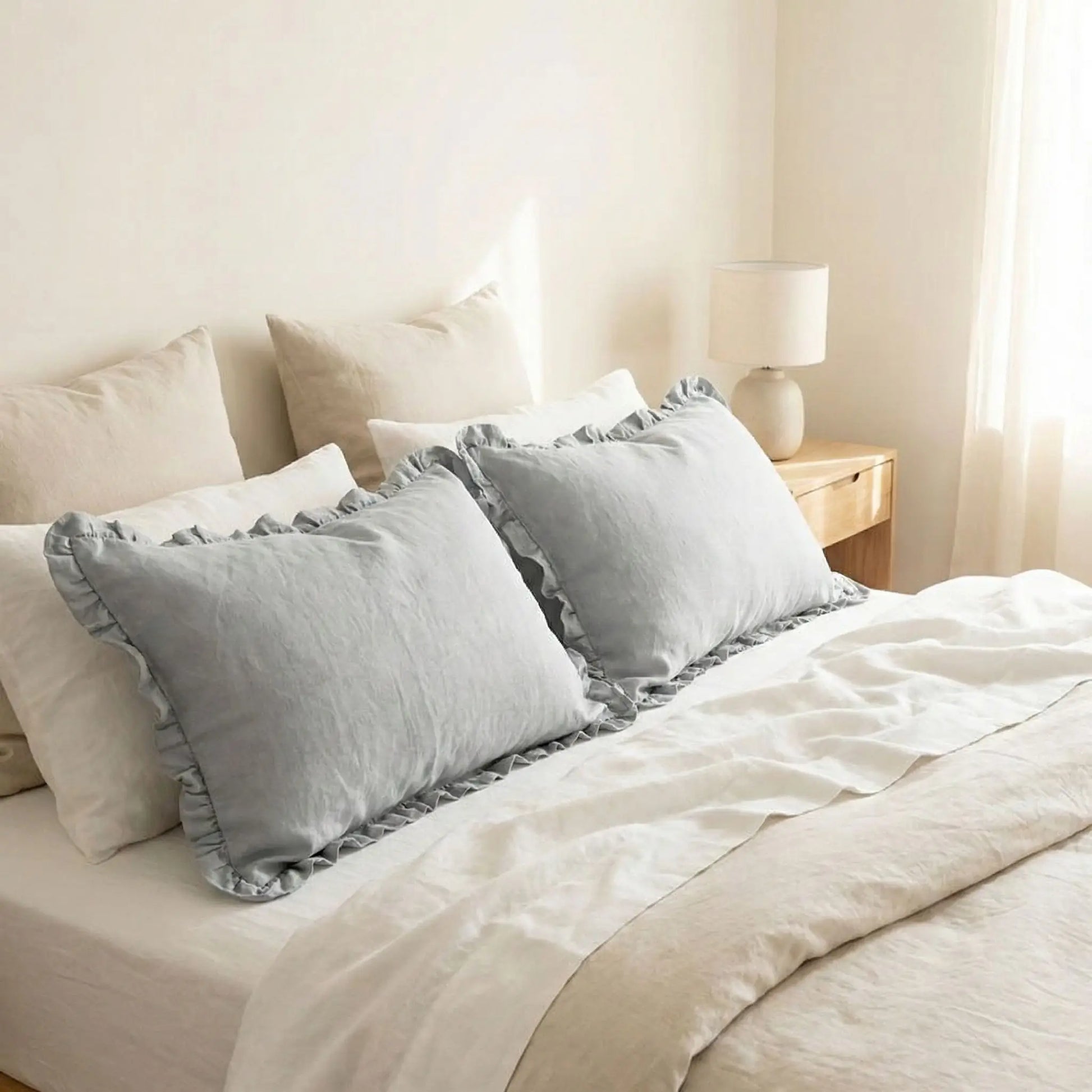 Taies d’oreiller en lin gris à volants posées sur un lit en bois clair avec linge de lit blanc cassé