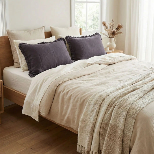 Taies d’oreiller en lin gris foncé à volants posées sur un lit en bois clair avec linge de lit blanc cassé