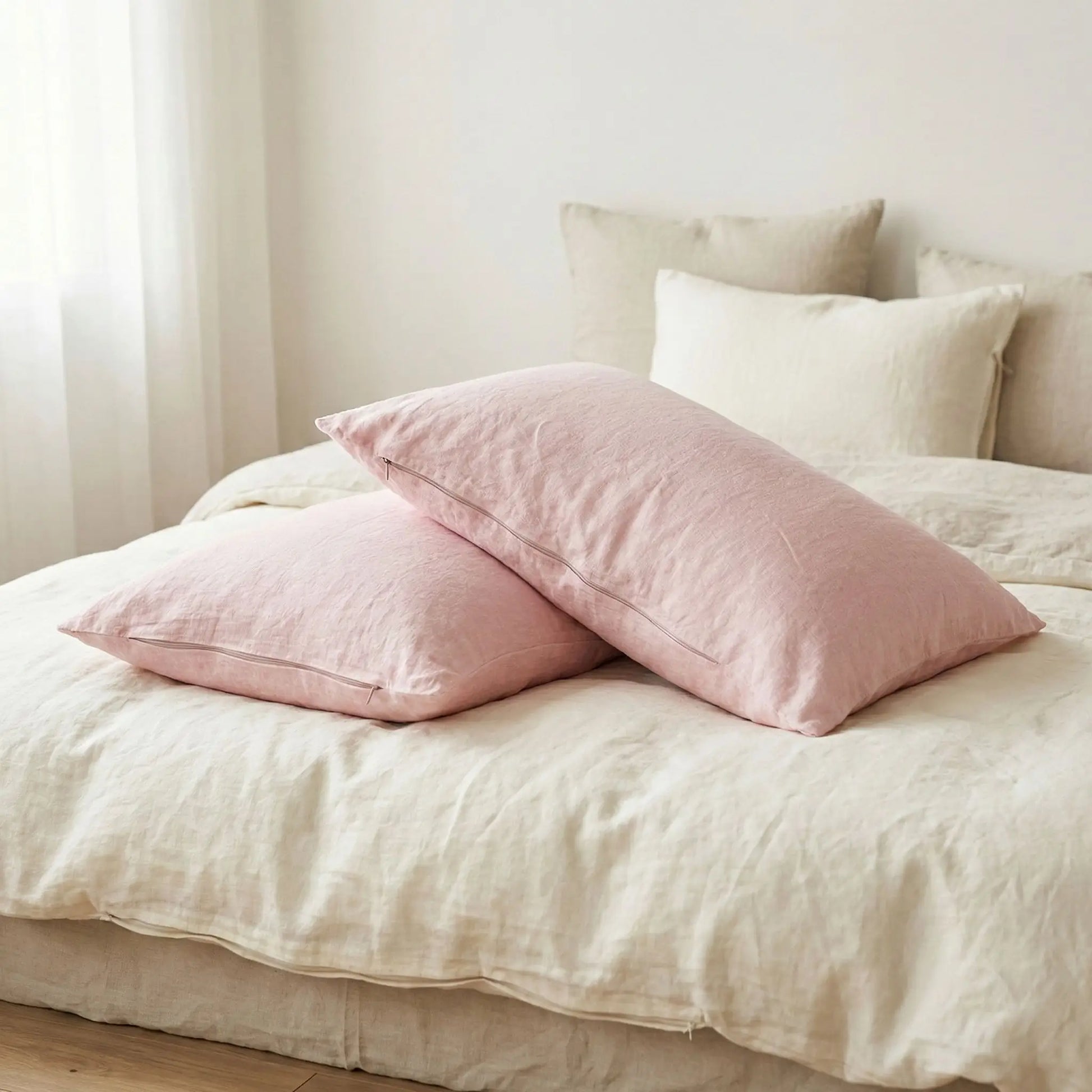 Taies d’oreiller en lin rose posées sur un lit en bois clair avec linge de lit blanc cassé 