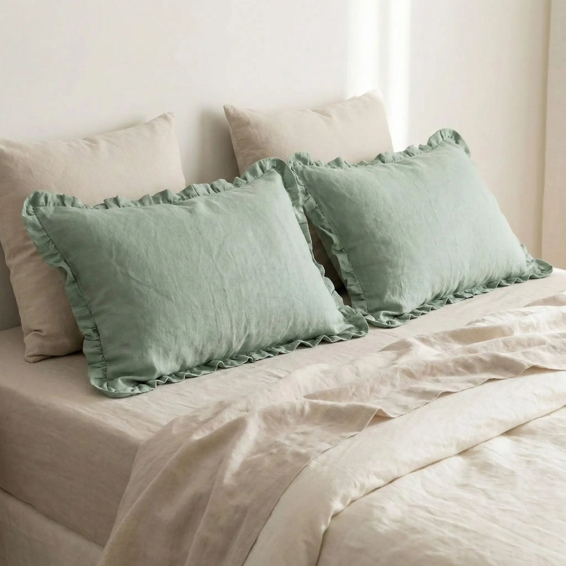 Taies d’oreiller en lin vert à volants posées sur un lit en bois clair avec linge de lit blanc cassé