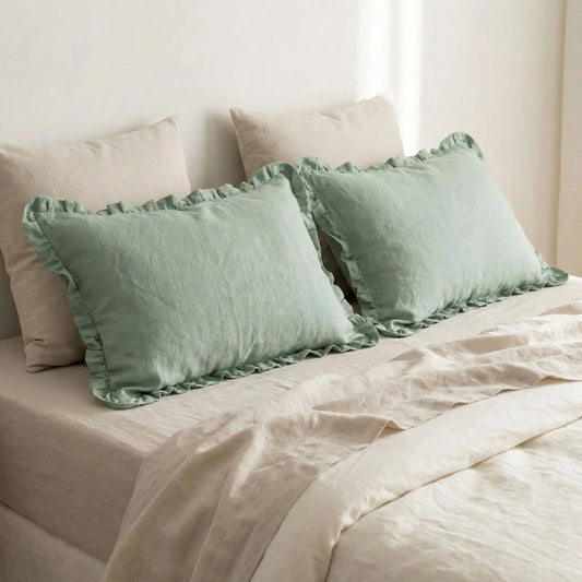 Taies d’oreiller en lin vert à volants posées sur un lit en bois clair avec linge de lit blanc cassé