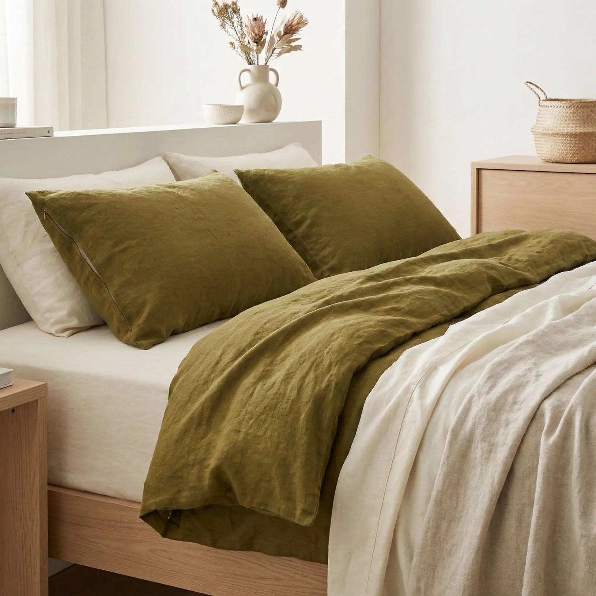 Taies d’oreiller en lin vert olive posées sur un lit en bois clair avec linge de lit blanc cassé