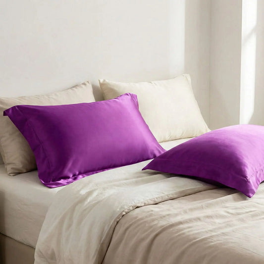 Taies d’oreiller en satin violet profond posées sur un lit en bois clair avec linge de lit blanc cassé ambiance lumineuse et naturelle