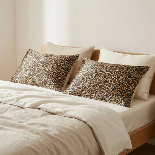 Taies d’oreiller en soie à motif ambre sauvage posées sur un lit en bois clair avec linge de lit blanc casséclair