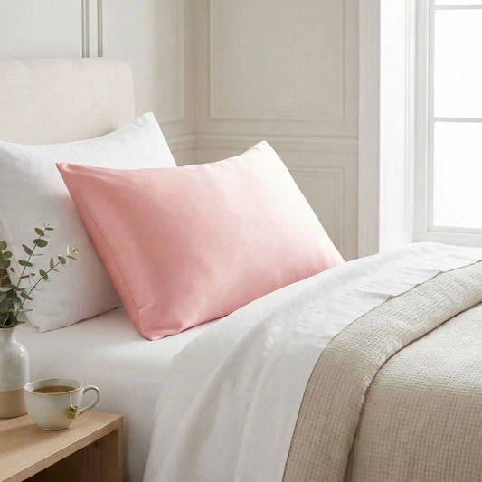 Taies d’oreiller en soie de mûrier rose posées sur un lit en bois clair avec linge de lit blanc cassé ambiance lumineuse et naturelle