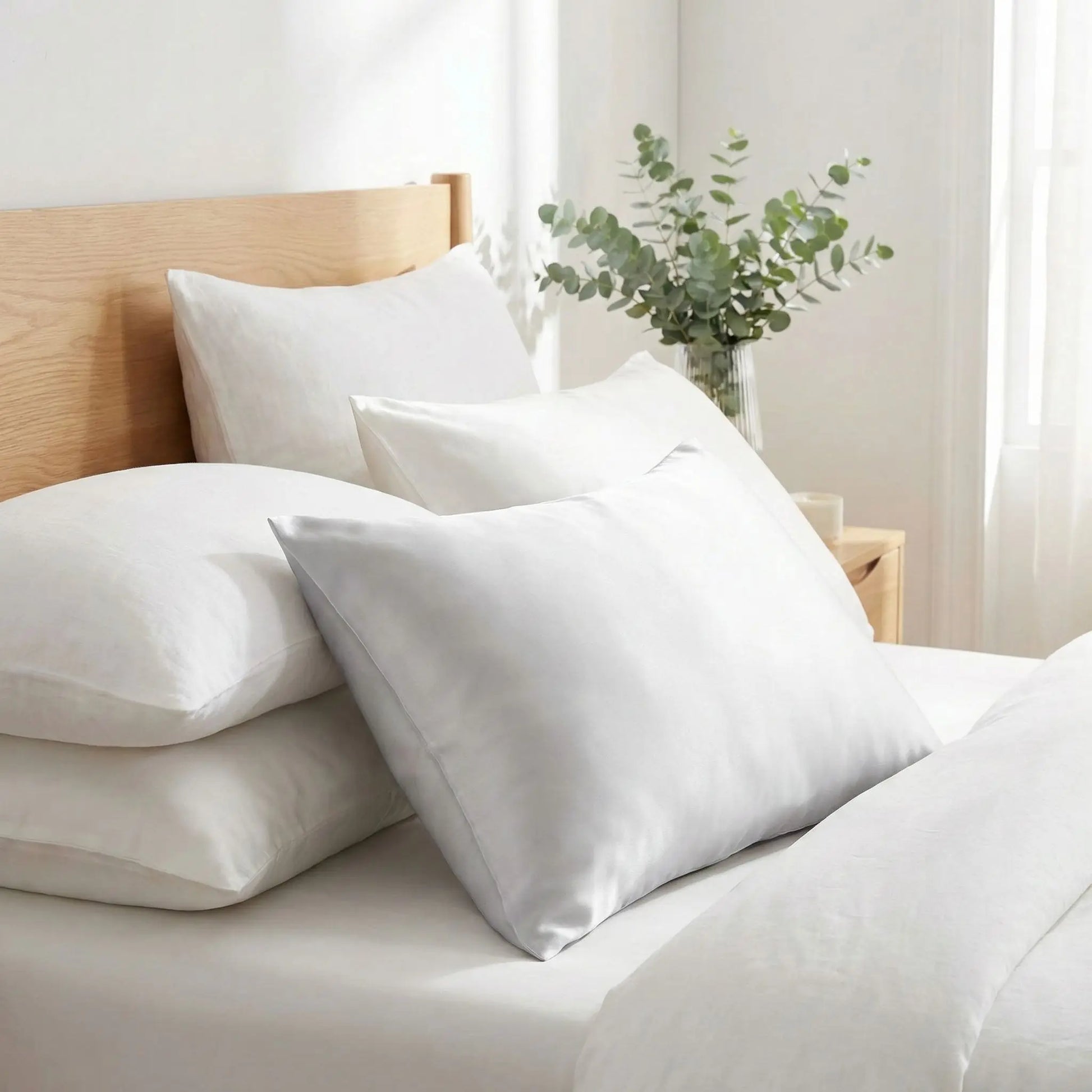 Taies d’oreiller en soie de mûrier 25 mommes blanches posées sur un lit en bois clair avec linge de lit blanc cassé ambiance lumineuse et naturelle