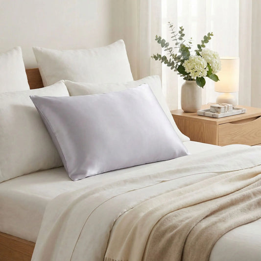 Taies d’oreiller en soie de mûrier grise posées sur un lit en bois clair avec linge de lit blanc cassé ambiance lumineuse et naturelle