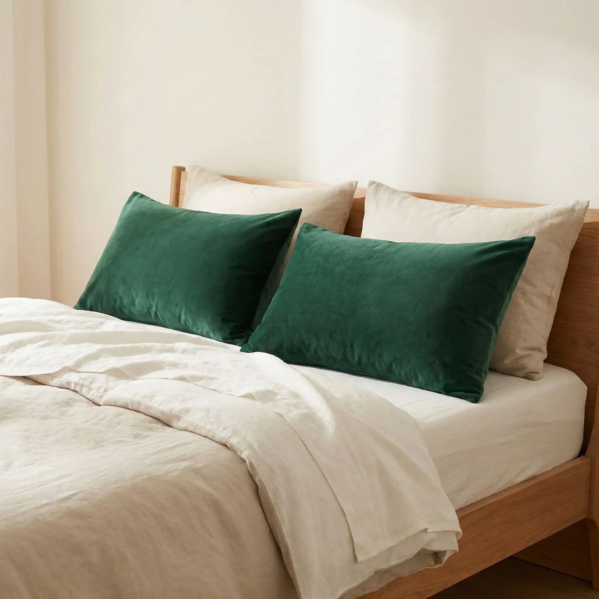 Taies d’oreiller en velours vert posées sur un lit en bois clair avec linge de lit blanc cassé