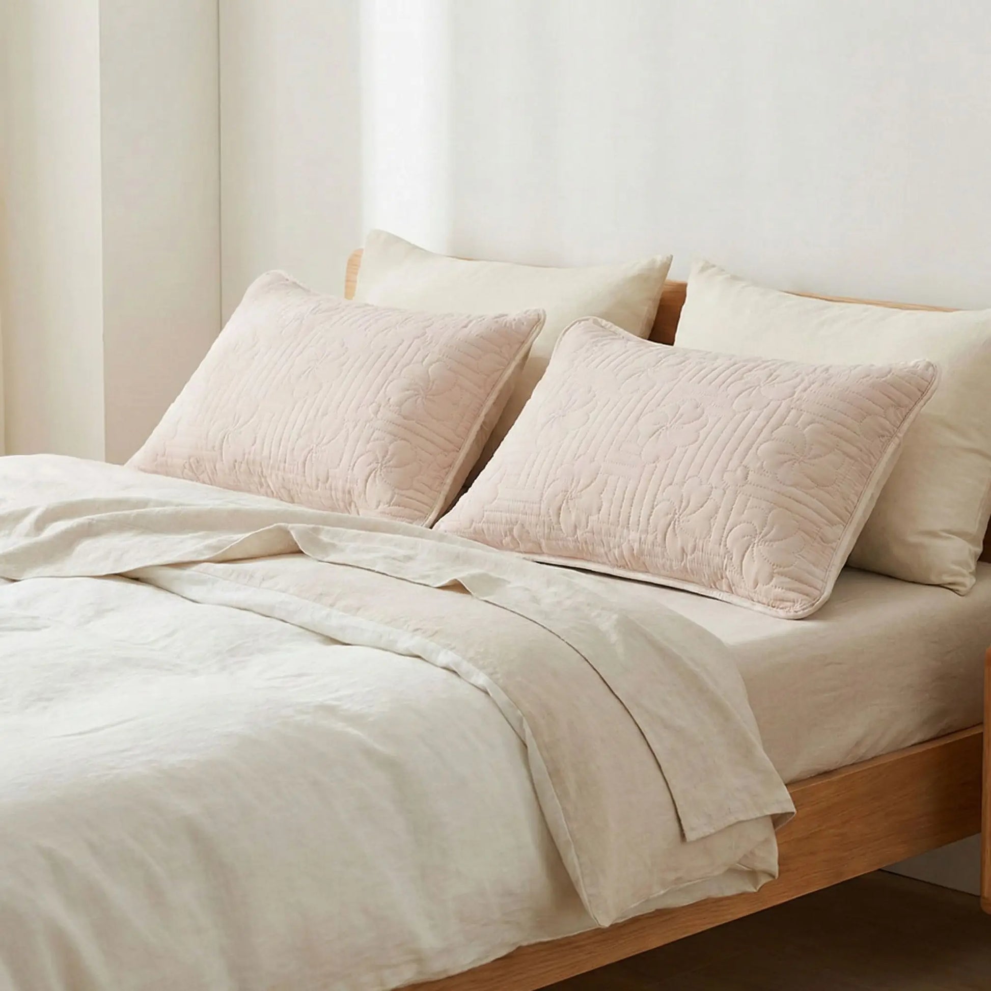 Taies d’oreiller imperméables beige posées sur un lit en bois clair avec linge de lit blanc cassé