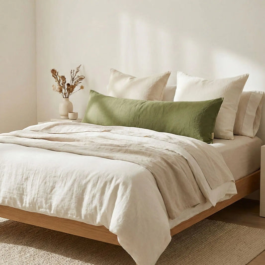 Taies de traversin en lin vert avocat posées sur un lit en bois clair avec linge de lit blanc cassé