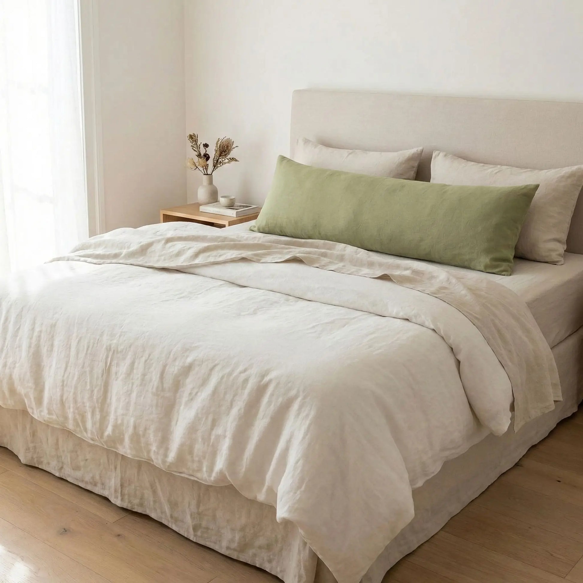 Taies de traversin en lin vert pois posées sur un lit en bois clair avec linge de lit blanc cassé