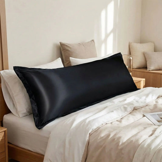 Taies de traversin en satin noir posées sur un lit en bois clair avec linge de lit blanc cassé