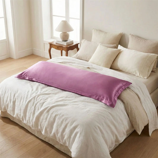 Taies de traversin en satin violet mauve posées sur un lit en bois clair avec linge de lit blanc cassé