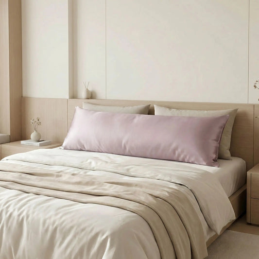 Taies de traversin en soie de mûrier mauve perle posées sur un lit en bois clair avec linge de lit blanc cassé