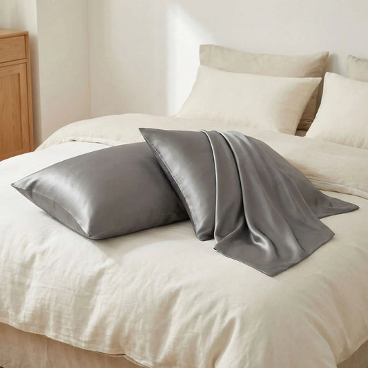 Taies d’oreiller en soie de mûrier 22 mommes grises posées sur un lit en bois clair avec linge de lit blanc cassé ambiance lumineuse et naturelle